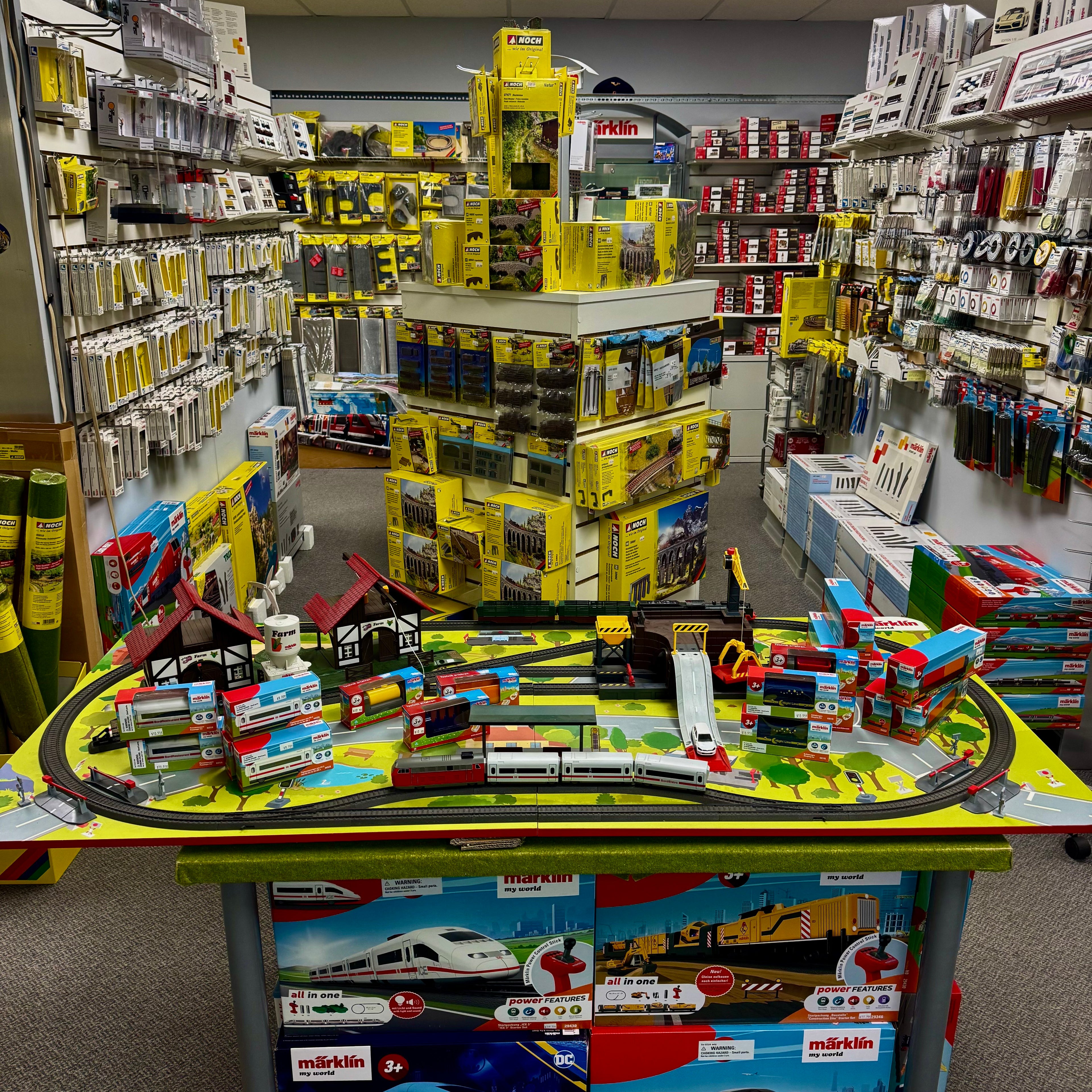 Toy train set on a table with shelves of model train parts in the background